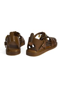 Braune Leder-Sandalen mit offenem Design, mehreren Riemen, verstellbaren Schnallen und einer strukturierten Sohle. Akzente umfassen kleine dekorative Münzen.
