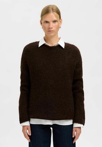Suéter de punto marrón con cuello redondo y mangas largas, superpuesto a una camisa blanca con cuello. Textura suave y ajuste relajado.