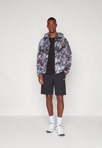 Lett jakke i svart og grått abstrakt mønster, med hette og snorer. Kombinert med svarte shorts og hvite joggesko.