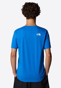 Blå kortärmad t-shirt i bomull, med en rundad halsringning och en liten vit logotyp på den övre ryggen. Slät textur.