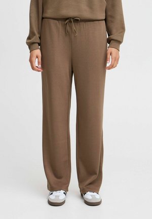 Brown, loose-fitting pants made of soft fabric with an elastic waistband and drawstring. Paired with white sneakers featuring gray accents.