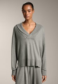 Maglione grigio lavorato a maglia con scollo a V e colletto a scialle, con maniche lunghe e un orlo che arriva leggermente al di sotto della vita.