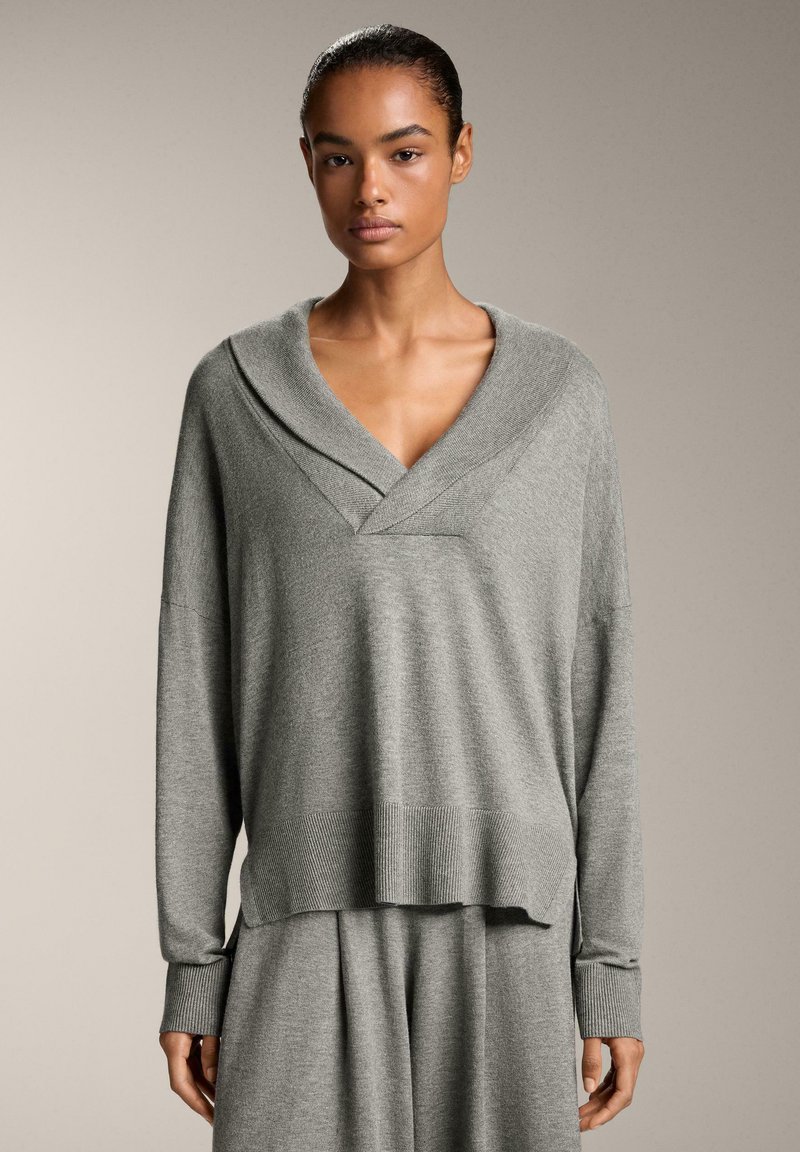 Maglione grigio lavorato a maglia con scollo a V e colletto a scialle, con maniche lunghe e un orlo che arriva leggermente al di sotto della vita.