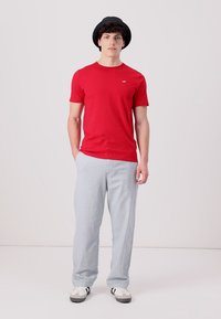 Camiseta roja de manga corta, corte relajado, material de algodón. Combinada con pantalones grises claros, textura suave, corte recto y calzado informal.