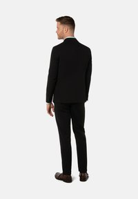 Schwarzer Anzug mit schlanker Passform, einreihig mit einem Reverskragen. Maßgeschneiderte Hose und braune Lederschuhe runden den Look ab.