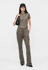 Γυναίκα που φοράει πράσινο-ελιά crop t-shirt και αντίστοιχο παντελόνι φόρμας, μαύρο καπέλο, μαύρη τσάντα στον ώμο και μαύρα μυτερά παπούτσια.