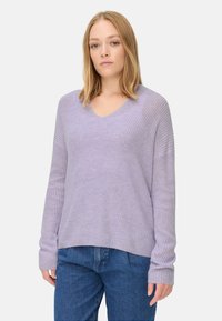 Helle lila Strickjacke mit V-Ausschnitt, gerippter Textur und langen �Ärmeln. Kombiniert mit blauen Jeans im lässig oversized Schnitt.