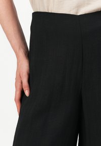 Pantaloni neri realizzati in un tessuto leggero, con una vita alta e tasche frontali, caratterizzati da una texture liscia e cuciture pulite.