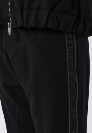Joggers negros con una franja lateral texturizada y cintura elástica. La tela parece suave, con un acabado general liso.