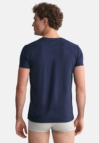 T-paita, jossa on lyhyet hihat ja tummansininen väri, valmistettu pehmeästä puuvillasta, klassisella pyöreällä kaula-aukolla ja slim fit -mallilla, nähtynä takaa.