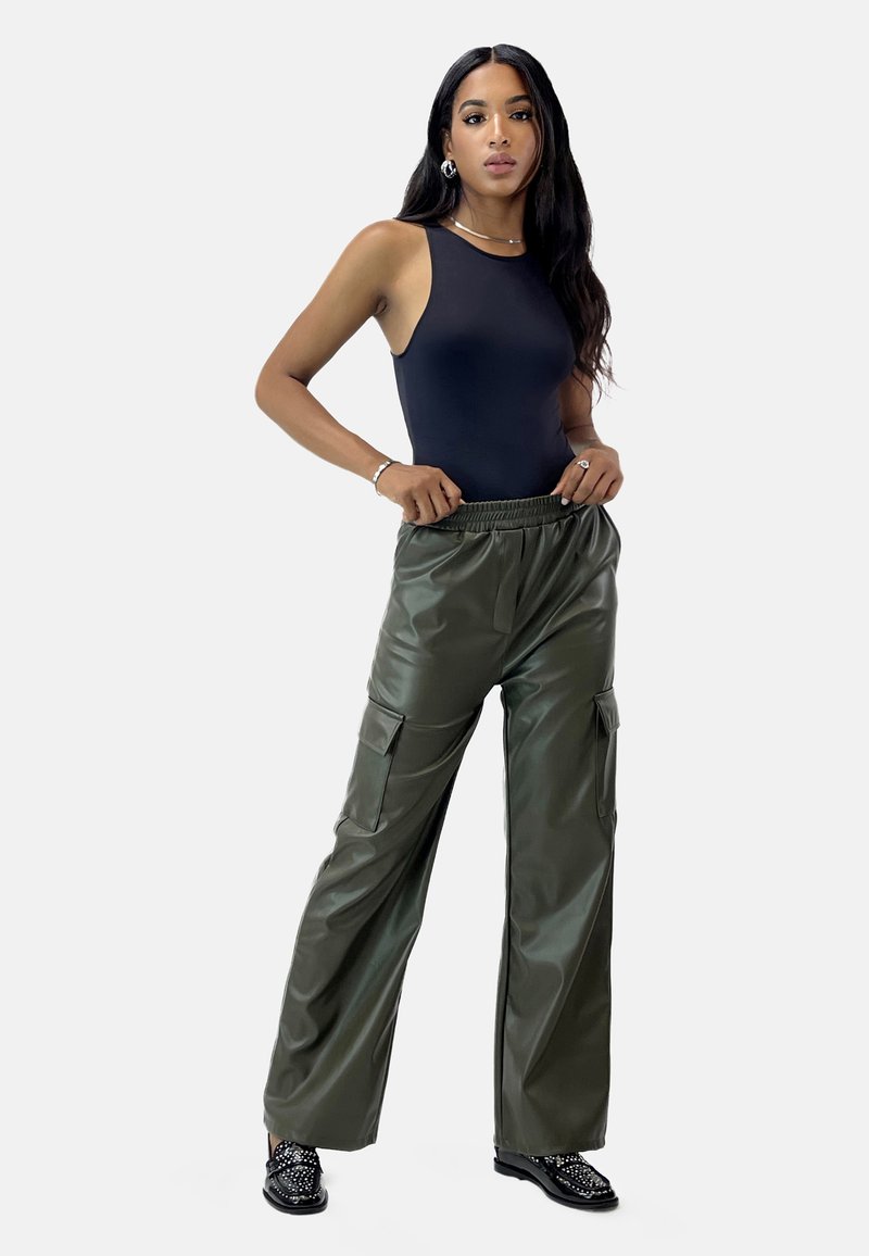 Svart ärmlös bodysuit, olivgrön imitationsläder vida cargobyxor med sidofickor, svarta utsmyckade platta skor, minimal smyckessättning.