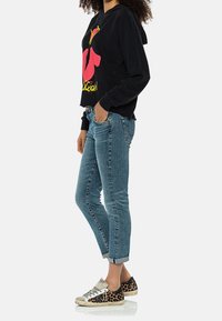 Sudadera negra con un diseño gráfico vibrante en rosa y amarillo, combinada con jeans de tiro alto en azul claro y zapatillas de leopardo.