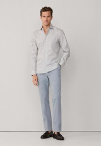 Langärmliges Button-Up-Hemd mit dünnen grauen und weißen vertikalen Streifen, kombiniert mit hellblauen Slim-Fit-Hosen und schwarzen Dressschuhen.