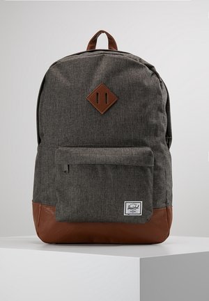 Sac à dos en tissu gris avec un fond en cuir marron et des accents, poche zippée à l'avant et petit patch blanc avec le logo Herschel.