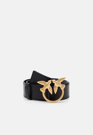 Ceinture en cuir noir roulée avec une boucle circulaire dorée représentant deux oiseaux détaillés se faisant face en plein vol.