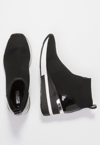 Zwarte sneakerboots hebben een gebreide bovenkant, een elastische enkel en een slanke wiggenhak met een glanzend zwart accent en witte zolen.