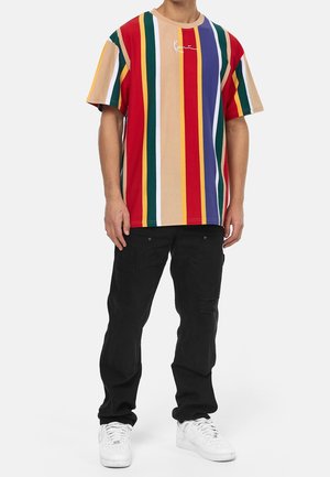 Multifarvet stribet T-shirt i rød, grøn, gul og blå med rund halsudskæring. Sammen med sorte bukser og hvide sneakers.