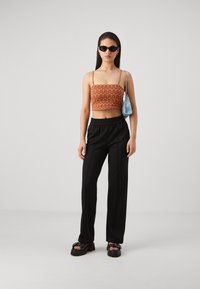 Black wide-leg trousers, orange patterned cropped top, and chunky black platform sandals. Complete with small blue handbag and sunglasses.