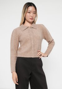 Lys brun strikket cardigan med krage, som har en vertikal rad av dekorative knapper og subtile teksturer. Lange ermer, kortere passform.
