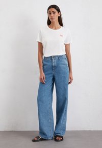 White, short-sleeve t-shirt with "You" printed in red, paired with loose-fitting, high-waisted light blue jeans and black sandals.