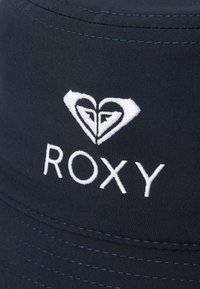 Marineblauwe bucket hat van zachte stof met een geborduurd wit logo met hartmotieven en het woord "ROXY" aan de voorkant.