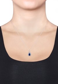 Silberne Halskette mit einem tropfenförmigen blauen Edelstein in der Mitte, umgeben von kleineren klaren Steinen, die an einer dünnen Kette befestigt ist.