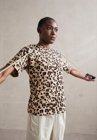 Tričko s leopardím potiskem v béžové barvě, s krátkými rukávy a volným střihem. Nenošené s béžovými šňůrkami, které zdůrazňují jeho pohodlný design.