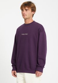 Sweat-shirt violet en coton avec un col rond et des poignets côtelés. Présente le logo "VOLCOM" en blanc, design minimaliste.