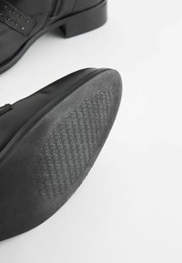 Czarnoskórzane buty z okrągłym czubkiem, ozdobione perforacjami, z niskim obcasem i teksturowaną gumową podeszwą dla lepszej przyczepności.