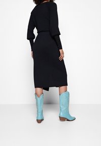 Robe noire à manches longues avec une taille cintrée, assortie à des bottes de cowboy bleu clair ornées de coutures complexes et d'un bout pointu.