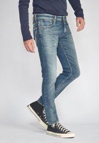 Vervaagde blauwe jeans met een slim fit, voorzien van vijf zakken, contrasterende stiksels en een rits. Gecombineerd met zwarte hoge sneakers.