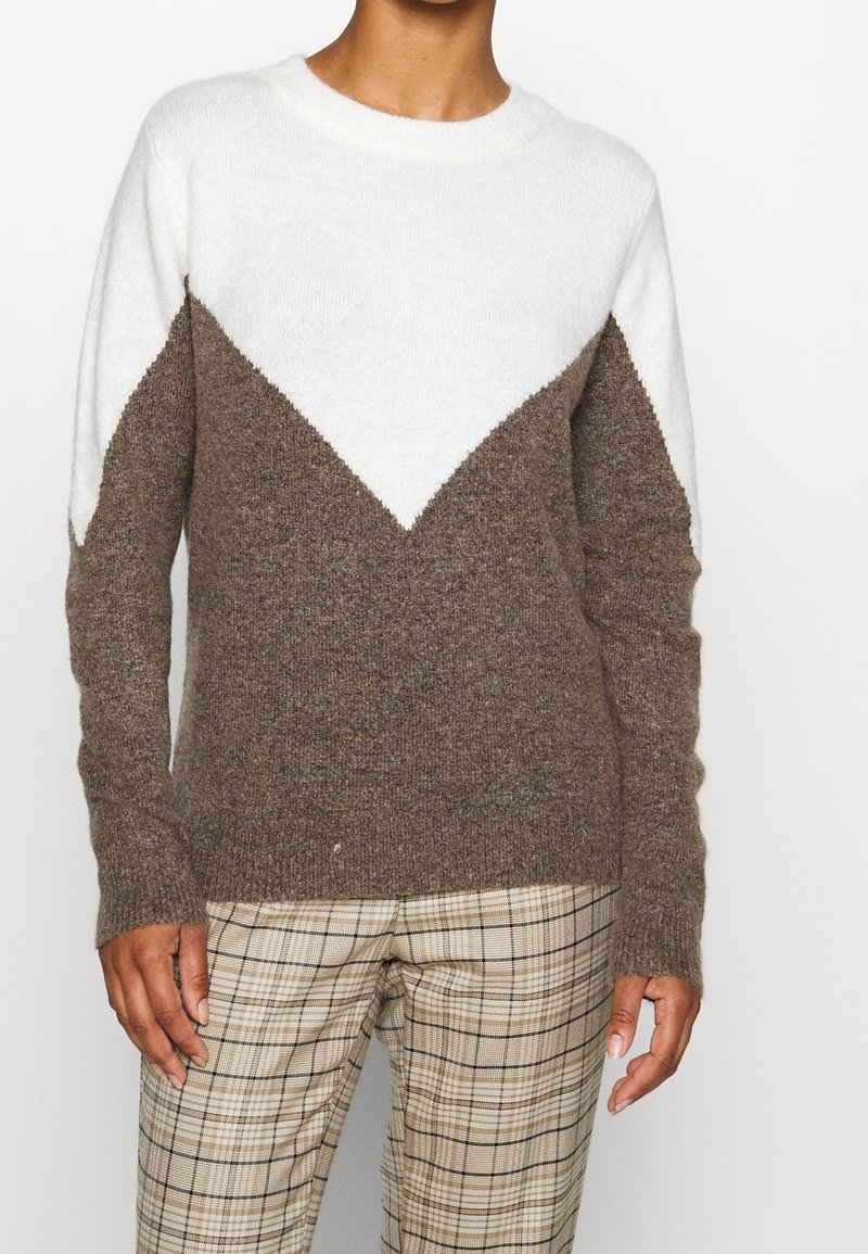 Brun och vit stickad tröja med en chevron-design, rund halsringning och långa ärmar, tillsammans med rutig byxor.