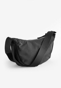 Zwarte stoffen schoudertas met een soepele textuur, voorzien van een ritsluiting en een verstelbare geribbelde schouderband voor comfortabel dragen.