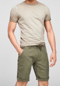 T-shirt beige à col rond avec manches retroussées, associée à un short en lin vert olive avec taille à cordon et ourlets retroussés.