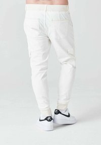 Pantalones cargo blancos de corte ajustado, con múltiples bolsillos. Combinados con zapatillas blancas con detalles negros y una cinturilla texturizada.