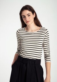 Gestreiftes Langarmshirt in Creme und Schwarz mit rundem Ausschnitt. Kombiniert mit einem hochgeschnittenen schwarzen Rock mit gebundenem Taillenzug.