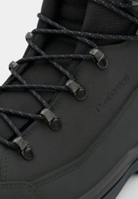 Grauer Wanderstiefel mit einer strukturierten Oberseite, ausgestattet mit dunklen Schnürsenkeln und Metallakzenten. Die Sohle ist robust und für unebenes Gelände konzipiert.