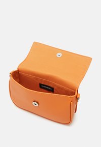 Bolso de mano naranja hecho de material sintético suave. Cuenta con un cierre de botón y un diseño interior simple con una etiqueta de la marca.