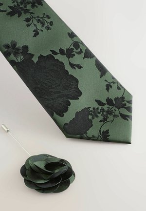 Grüne Krawatte mit schwarzem Blumenmuster, strukturierter Stoff, schräger Schnitt. Enthält eine schwarze Stoff-Reversnadel in Blumenform.