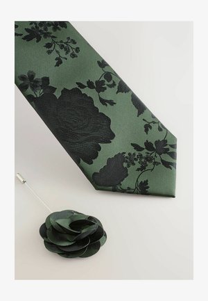 Grüne Krawatte mit schwarzem Blumenmuster, strukturierter Stoff, schräger Schnitt. Enthält eine schwarze Stoff-Reversnadel in Blumenform.