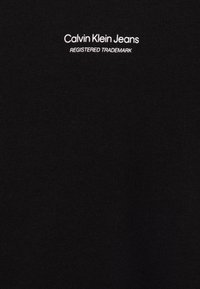 Czarna bawełniana koszulka z krótkim rękawem z białym haftowanym napisem "Calvin Klein Jeans" oraz "ZAREJESTROWANY ZNAK TOWAROWY" w okolicy dekoltu. Prosty wzór.
