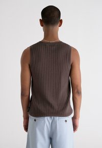 Brown ribbed sleeveless top with a crew neckline, worn with light blue pants, showcasing a textured fabric and fitted design.