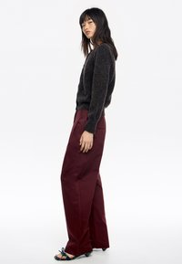 Suéter de punto gris oscuro con escote en V, combinado con pantalones de pierna ancha burdeos. El calzado presenta un diseño floral azul decorativo.