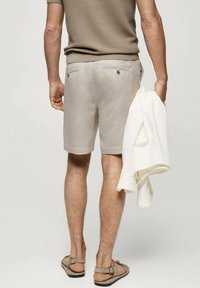 Shorts beige clair avec poches arrière, assortis à une veste crème claire. La tenue est complétée par des sandales marron et un tissu texturé.
