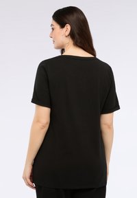 Camiseta negra de manga corta hecha de una tela suave, con cuello redondo y mangas enrolladas, de ajuste relajado y con una textura suave.