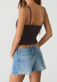 Top corto ajustado de tirantes finos en color marrón oscuro combinado con shorts de mezclilla azul claro con dobladillo deshilachado y bolsillos traseros con parche.