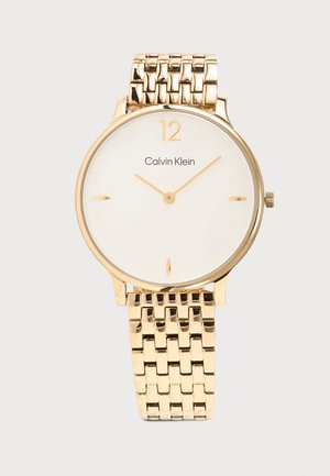 Montre-bracelet Calvin Klein dorée avec cadran blanc minimaliste, index des heures dorés à 12, 3, 6, 9, et bracelet à maillons dorés assortis.