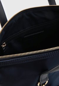 Granatowa torba na ramię o gładkiej powierzchni, złotym zamku błyskawicznym oraz wewnętrznej kieszeni na zamek. Podwójne skórzane uchwyty do noszenia.