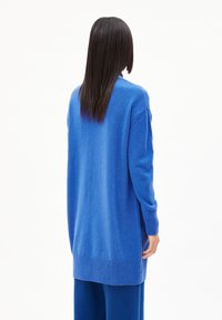 Lange blauwe cardigan van zacht materiaal, met geribbelde manchetten en onderrand, met een relaxed fit en zijsplitten voor meer bewegingsvrijheid.