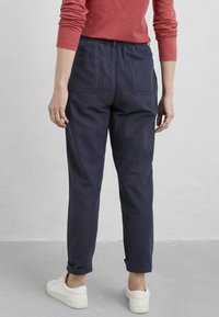 Marinblå, lätta bomullbyxor med avslappnad passform, elastisk midja, uppvikta ärmar och två bakt pockets. Bärs med vita sneakers.